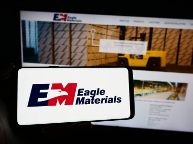 Stuttgart, Almanya - 02-23-2024: ABD 'li inşaat şirketi Eagle Materials Inc.' in logosuyla cep telefonu tutan kişi iş sayfasının önünde. Telefon ekranına odaklan.