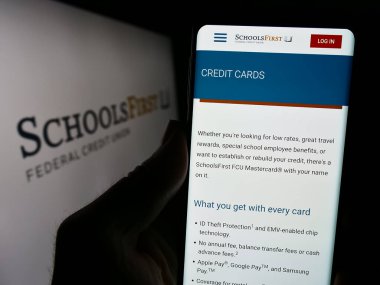 Stuttgart, Almanya - 02-23-2024: ABD 'li finans şirketi SchoolsFirst Federal Kredi Birliği' nin logolu web sayfası ile cep telefonu tutan kişi. Telefon ekranının merkezine odaklan.