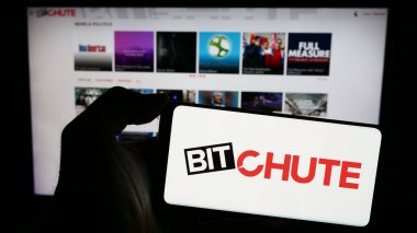 Stuttgart, Almanya - 02-23-2024: Video sunucu şirketi Bitchute 'un logosuyla cep telefonu sahibi kişi iş sayfasının önünde. Telefon ekranına odaklan.