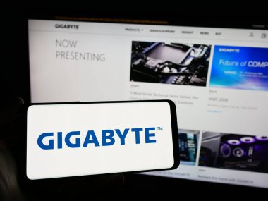 Stuttgart, Almanya - 02-24-2024: Tayvanlı bilgisayar donanım şirketi Gigabyte Technology 'nin logosuna sahip cep telefonu sahibi kişi web sayfasının önünde. Telefon ekranına odaklan.