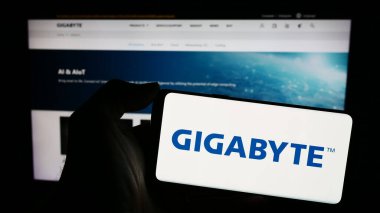 Stuttgart, Almanya - 02-24-2024: Tayvanlı bilgisayar donanım şirketi Gigabyte Technology 'nin logosunun bulunduğu cep telefonu sahibi kişi web sayfası önünde. Telefon ekranına odaklan.