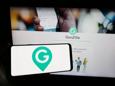 Stuttgart, Almanya - 02-24-2024: İnternet sitesi önünde ABD GPS izleme şirketi GeoZilla Inc. 'in logosuna sahip akıllı telefon sahibi kişi. Telefon ekranına odaklan.