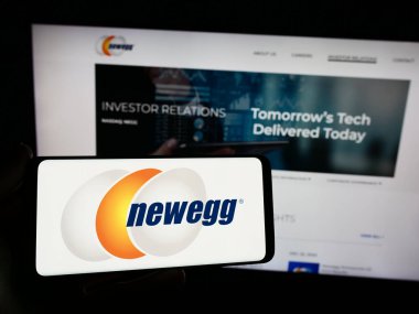 Stuttgart, Germany - 02-24-2024: Person holding smartphone with logo of US computer retail company Newegg Commerce Inc. in front of website. Focus on phone display. clipart