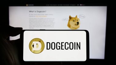Stuttgart, Almanya - 02-26-2024: İnternet sayfası önünde şifreli Dogecoin logosu bulunan kişi. Telefon ekranına odaklan.