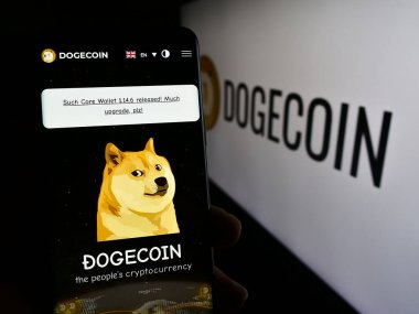Stuttgart, Almanya - 02-26-2024: Logonun önünde şifreli para birimi Dogecoin web sayfası olan akıllı telefonu elinde tutan kişi. Telefon ekranının merkezine odaklan.