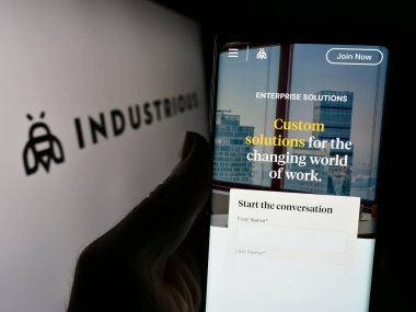 Stuttgart, Almanya - 02-26-2024: İş logosu önünde çalışan ABD 'li ortak uzay şirketi Industrious' un web sayfası ile akıllı telefon tutan kişi. Telefon ekranının merkezine odaklan.