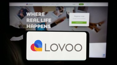 Stuttgart, Almanya - 02-26-2024: İş sayfasının önünde Alman online flört platformu LOVOO 'nun logosu olan cep telefonu sahibi kişi. Telefon ekranına odaklan.