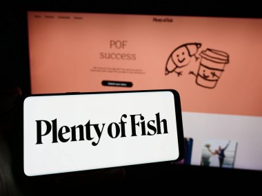 Stuttgart, Almanya - 02-26-2024: İnternet sayfası önünde Kanadalı randevu şirketi Plentyoffish Media ULC 'nin logosu olan cep telefonu sahibi kişi. Telefon ekranına odaklan.