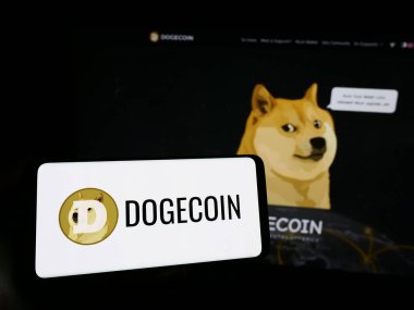 Stuttgart, Almanya - 02-26-2024: İnternet sayfasının önünde şifreli para birimi Dogecoin logosu bulunan cep telefonu sahibi kişi. Telefon ekranına odaklan.
