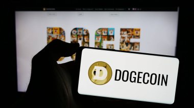 Stuttgart, Almanya - 02-26-2024: İnternet sitesinin önünde şifreli para birimi Dogecoin logosu taşıyan kişi. Telefon ekranına odaklan.