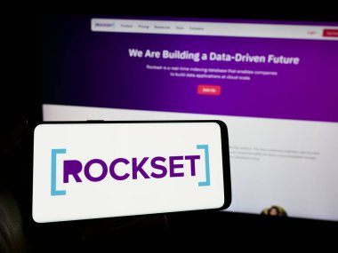 Stuttgart, Germany - 02-29-2024: Person holding cellphone with logo of US analytics database company Rockset Inc. in front of business webpage. Focus on phone display. clipart