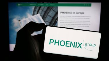 Stuttgart, Almanya - 03-01-2024: Alman ilaç firması PHOENIX Pharmahandel 'in logosuna sahip akıllı telefon sahibi kişi web sitesinin önünde. Telefon ekranına odaklan.