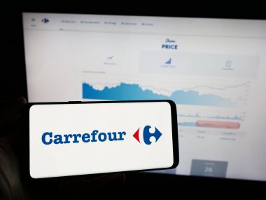 Stuttgart, Almanya - 03-01-2024: Fransız perakende şirketi Carrefour S.A. 'nın logosuyla cep telefonu sahibi kişi iş sayfasının önünde. Telefon ekranına odaklan.