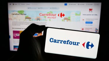 Stuttgart, Germany - 03-01-2024: Person holding smartphone with logo of French retail company Carrefour S.A. in front of website. Focus on phone display. clipart