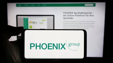 Stuttgart, Almanya - 03-01-2024: Üzerinde Alman ilaç firması PHOENIX Pharmahandel 'in logosu bulunan cep telefonu sahibi kişi iş sayfası önünde. Telefon ekranına odaklan.