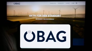 Stuttgart, Almanya - 03-14-2024: Avusturyalı Oesterreichische Beteiligungs AG (BAG) şirketinin logosunun bulunduğu cep telefonu sahibi kişi web sayfası önünde. Telefon ekranına odaklan.