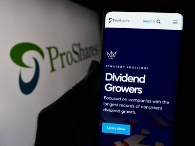 Stuttgart, Almanya - 03-15-2024: ABD 'li finans hizmetleri şirketi ProShares' ın internet sayfası ile iş logosu önünde cep telefonu tutan kişi. Telefon ekranının merkezine odaklan.