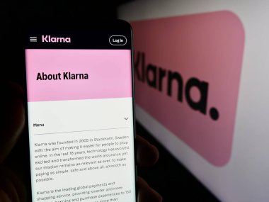 Stuttgart, Almanya - 03-16-2024: İsveçli fintech şirketi Klarna Bank AB 'nin internet sayfası ile iş logosu önünde cep telefonu tutan kişi. Telefon ekranının merkezine odaklan.