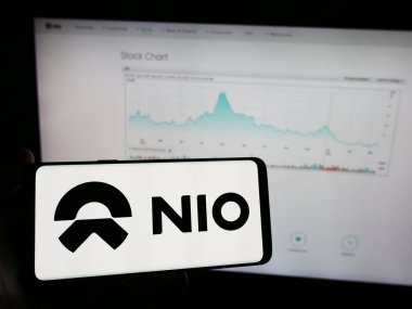 Stuttgart, Almanya - 03-16-2024: Çinli elektrikli taşıt şirketi Nio Inc. 'in logosunun bulunduğu cep telefonu sahibi kişi iş sayfasının önünde. Telefon ekranına odaklan.