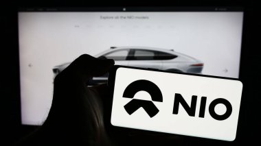 Stuttgart, Almanya - 03-16-2024: Çinli elektrikli araç şirketi Nio Inc. 'in logosuyla cep telefonu sahibi kişi iş sayfasının önünde. Telefon ekranına odaklan.