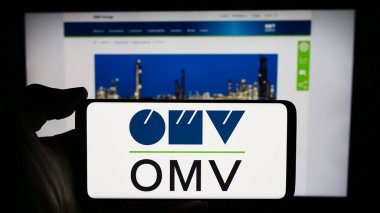 Stuttgart, Almanya - 03-16-2024: Avusturyalı petrol ve gaz şirketi OMV Aktiengesellschaft 'ın logosuna sahip akıllı telefon sahibi kişi web sitesinin önünde. Telefon ekranına odaklan.