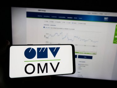 Stuttgart, Almanya - 03-16-2024: Avusturyalı petrol ve gaz şirketi OMV Aktiengesellschaft 'ın logosuna sahip cep telefonu sahibi kişi web sayfasının önünde. Telefon ekranına odaklan.