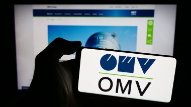 Stuttgart, Almanya - 03-16-2024: Avusturyalı petrol ve doğalgaz şirketi OMV Aktiengesellschaft 'ın logosunun bulunduğu cep telefonu sahibi kişi iş sayfasının önünde. Telefon ekranına odaklan.