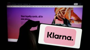Stuttgart, Almanya - 03-16-2024: İsveçli fintech şirketi Klarna Bank AB 'nin logosunun bulunduğu cep telefonu sahibi kişi iş sayfasının önünde. Telefon ekranına odaklan.