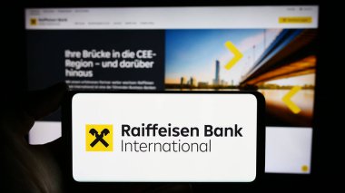 Stuttgart, Almanya - 03-16-2024: Avusturyalı firma Raiffeisen Bank International AG (RBI) logosunun bulunduğu cep telefonu sahibi kişi web sayfası önünde. Telefon ekranına odaklan.