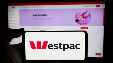 Stuttgart, Almanya - 03-16-2024: Avustralyalı finans şirketi Westpac Banking Corporation 'ın logosuyla cep telefonu tutan kişi web sayfası önünde. Telefon ekranına odaklan.