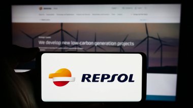 Stuttgart, Almanya - 03-16-2024: İş sayfası önünde İspanyol petrol şirketi Repsol S.A. 'nın logosuna sahip cep telefonu sahibi kişi. Telefon ekranına odaklan.