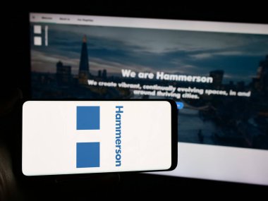 Stuttgart, Almanya - 03-16-2024: İngiliz emlak şirketi Hammerson plc 'nin logosuna sahip akıllı telefon sahibi kişi web sitesinin önünde. Telefon ekranına odaklan.