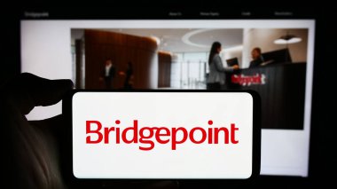 Stuttgart, Almanya - 03-16-2024: İngiliz yatırım şirketi Bridgepoint Group plc 'in logosuyla cep telefonu sahibi kişi iş sayfasının önünde. Telefon ekranına odaklan.