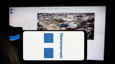 Stuttgart, Almanya - 03-16-2024: İngiliz emlak şirketi Hammerson plc 'nin logosuyla cep telefonu sahibi kişi iş sayfasının önünde. Telefon ekranına odaklan.