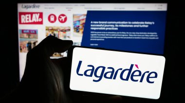 Stuttgart, Almanya - 03-17-2024: Fransız yayıncılık ve perakende şirketi Lagardere SA 'nın logosuna sahip cep telefonu sahibi kişi iş sayfasının önünde. Telefon ekranına odaklan.