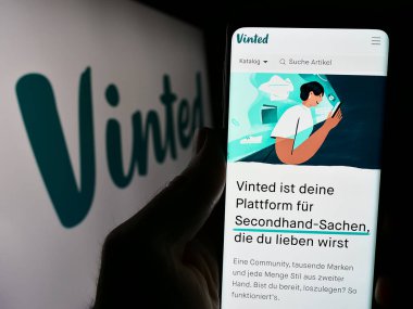 Stuttgart, Almanya - 03-17-2024: Logo önünde Vinted adlı çevrimiçi ikinci el pazar şirketinin web sayfası ile akıllı telefon tutan kişi. Telefon ekranının merkezine odaklan.