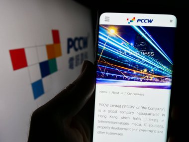 Stuttgart, Almanya - 03-17-2024: Telekomünikasyon şirketi PCCW Limited 'in web sayfası ile akıllı telefon sahibi kişi iş logosu önünde. Telefon ekranının merkezine odaklan.