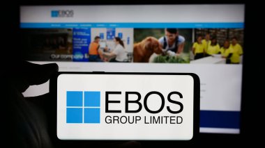 Stuttgart, Almanya - 03-17-2024: Üzerinde ilaç dağıtım şirketi EBOS Group Ltd. 'nin logosu bulunan cep telefonu sahibi kişi iş sayfasının önünde. Telefon ekranına odaklan.