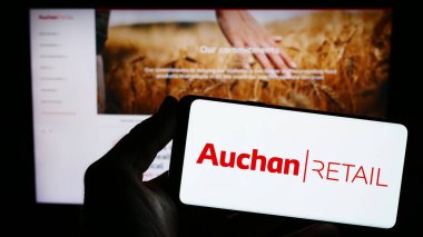 Stuttgart, Almanya - 03-05-2024: İnternet sitesi önünde Fransız Auchan Retail International S.A. şirketinin logosuna sahip kişi. Telefon ekranına odaklan.