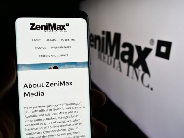 Stuttgart, Almanya - 03-05-2024: İş logosu önünde ABD 'li video oyunu şirketi ZeniMax Media Inc.' in web sayfası ile cep telefonu tutan kişi. Telefon ekranının merkezine odaklan.