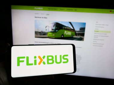 Stuttgart, Almanya - 03-05-2024: Busines web sayfası önünde üzerinde Alman uzun mesafe otobüs taşımacılığı şirketi FlixBus 'un logosu bulunan cep telefonu sahibi kişi. Telefon ekranına odaklan.