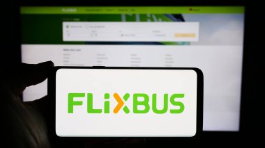 Stuttgart, Almanya - 03-05-2024: İş sayfası önünde Alman uzun mesafe otobüs taşımacılığı şirketi FlixBus 'un logosuyla cep telefonu tutan kişi. Telefon ekranına odaklan.