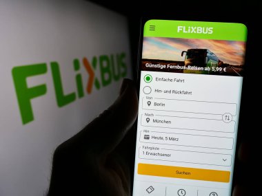 Stuttgart, Almanya - 03-05-2024: Logo önünde Alman uzun mesafe otobüs taşımacılığı şirketi FlixBus 'un internet sayfası ile cep telefonu tutan kişi. Telefon ekranının merkezine odaklan.