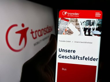Stuttgart, Almanya - 03-05-2024: Alman toplu taşıma şirketi Transdev GmbH 'nin internet sayfası ile logo önünde cep telefonu tutan kişi. Telefon ekranının merkezine odaklan.