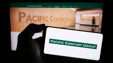Stuttgart, Almanya - 03-07-2024: Yatırım şirketi Pacific Century Group 'un (PCG) logosuna sahip cep telefonu sahibi kişi iş sayfasının önünde. Telefon ekranına odaklan.
