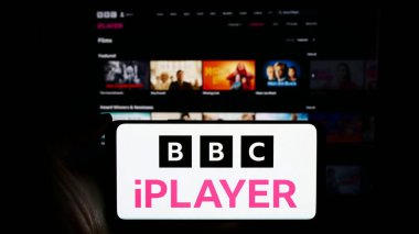 Stuttgart, Almanya - 03-07-2024: İş sayfası önünde BBC iPlayer talep servisi üzerinden İngiliz video logosuyla cep telefonu tutan kişi. Telefon ekranına odaklan.