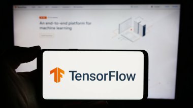 Stuttgart, Germany - 03-08-2024: Person holding cellphone with logo of open-source software library TensorFlow in front of webpage. Focus on phone display. clipart