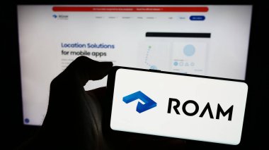 Stuttgart, Germany - 03-10-2024: Person holding mobile phone with logo of Dutch location tracking company Roam.ai in front of business web page. Focus on phone display. clipart