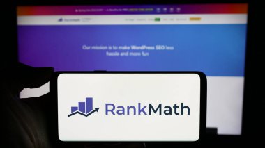Stuttgart, Almanya - 03-12-2024: Indian WordPress SEO şirketi Rank Math 'in logosuyla cep telefonu tutan kişi iş sayfası önünde. Telefon ekranına odaklan.