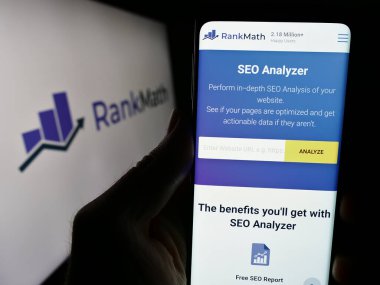 Stuttgart, Almanya - 03-12-2024: Indian WordPress SEO şirketi Rank Math 'in internet sayfası ile iş logosu önünde cep telefonu tutan kişi. Telefon ekranının merkezine odaklan.